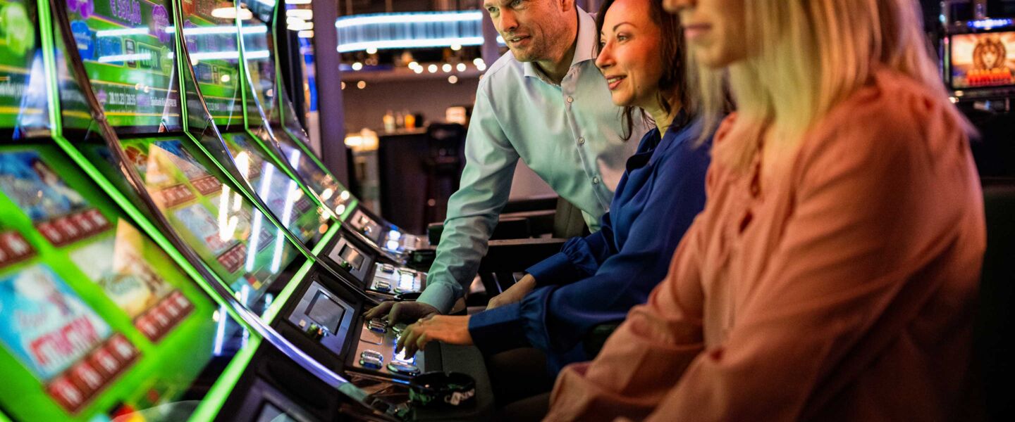 Zwei Frauen und ein Man spielen an Slot Machines.