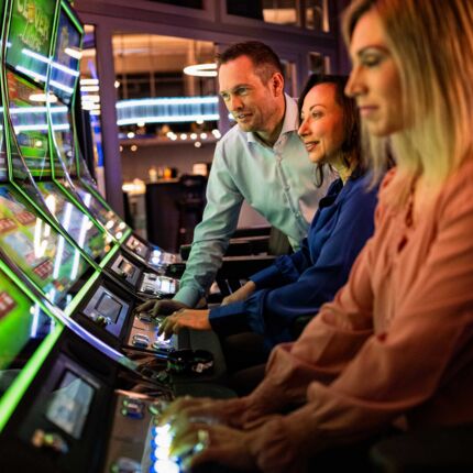 Zwei Frauen und ein Man spielen an Slot Machines.